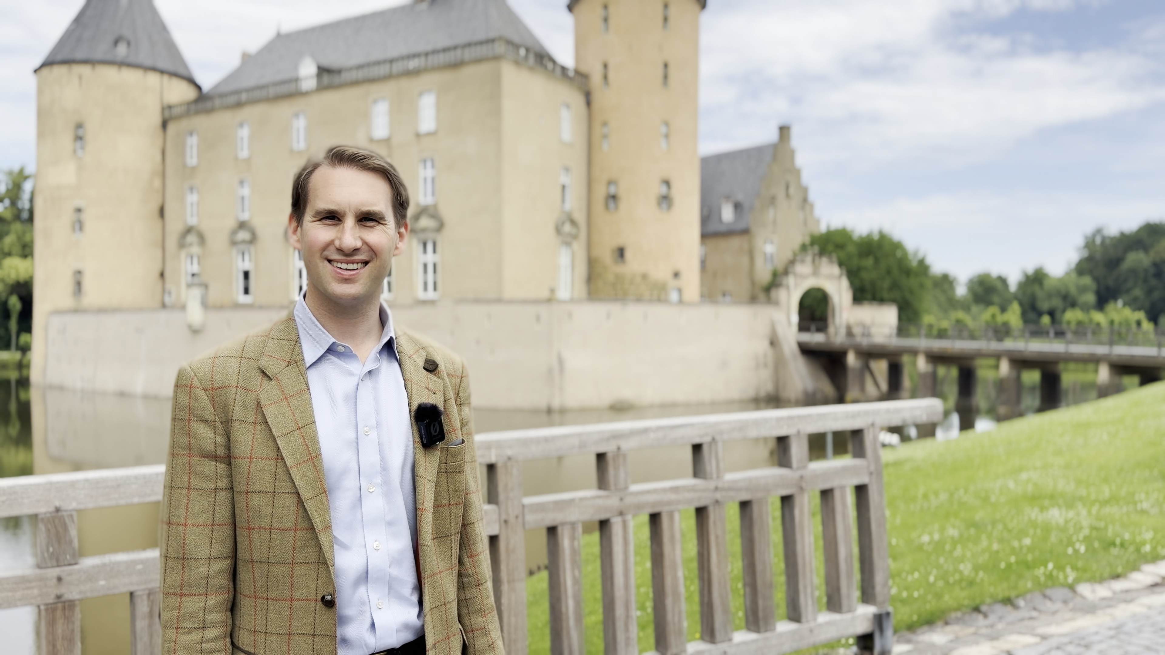 Ein Mann steht auf einem Weg am Wassergraben, der um eine Burg verläuft.