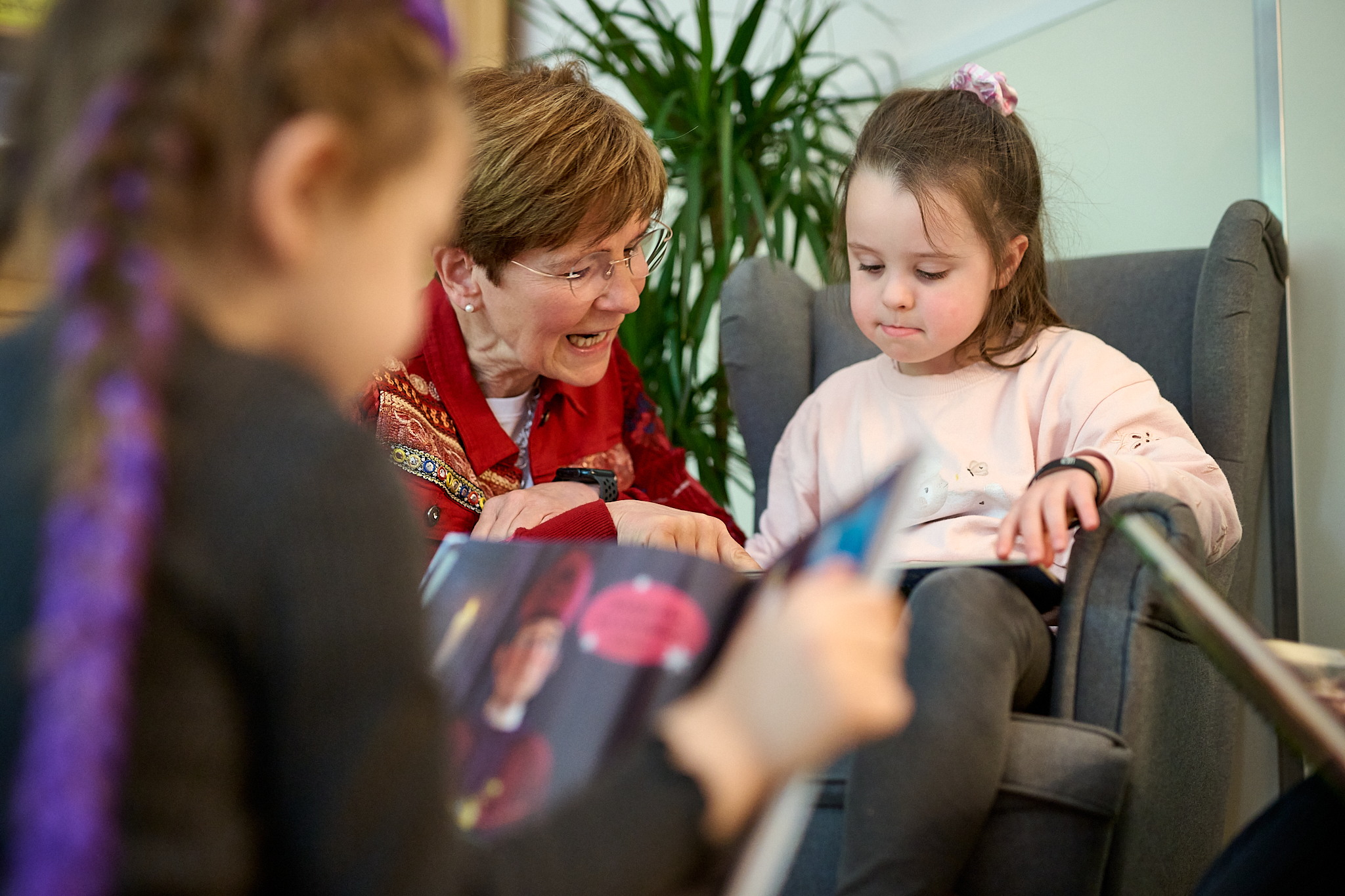 Eine Erzieherin liest gemeinsam mit Kindern. Ein Kind sitzt in einem kleinen Kindersessel.