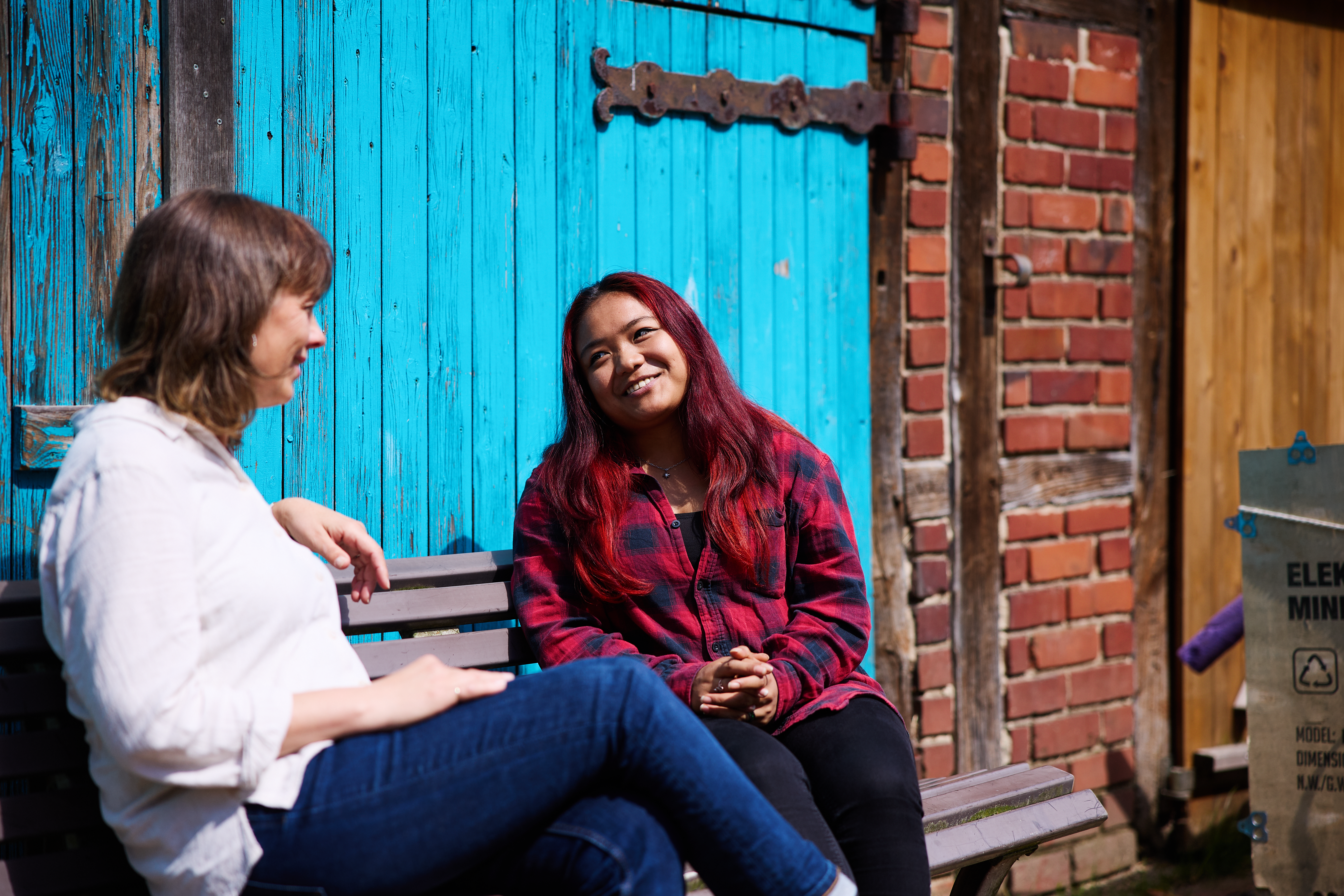 Zwei Frauen sitzen auf einer Bank für einem Scheunentor beim Haus Granat