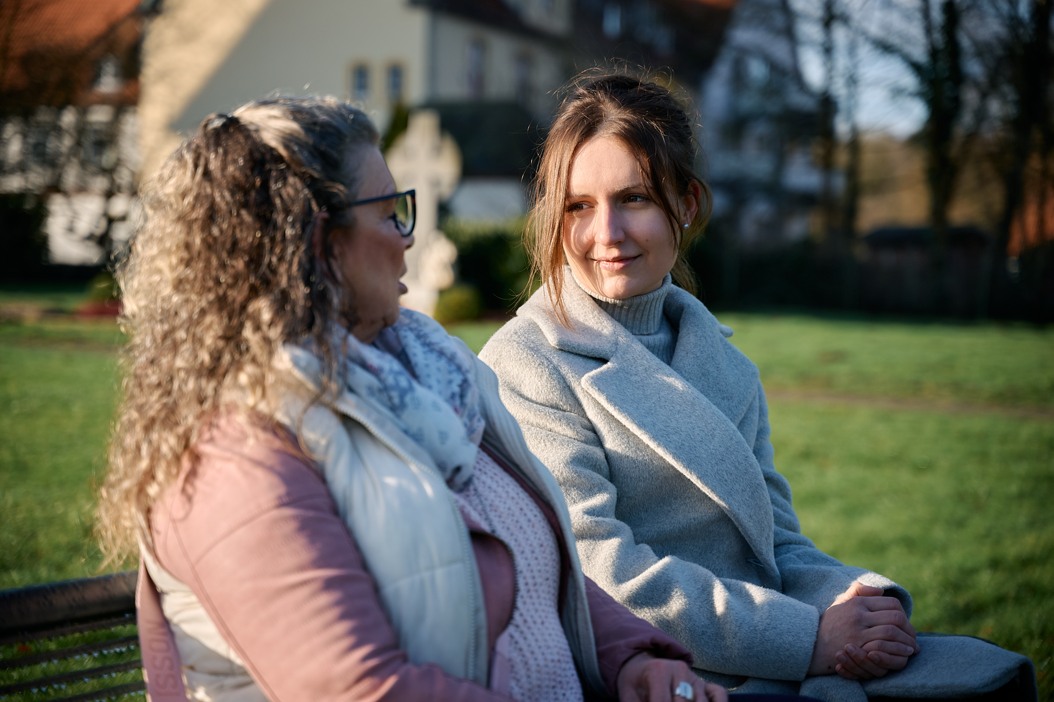 Zwei Frauen sitzen einander zugewandt auf einer Bank im Freien.
