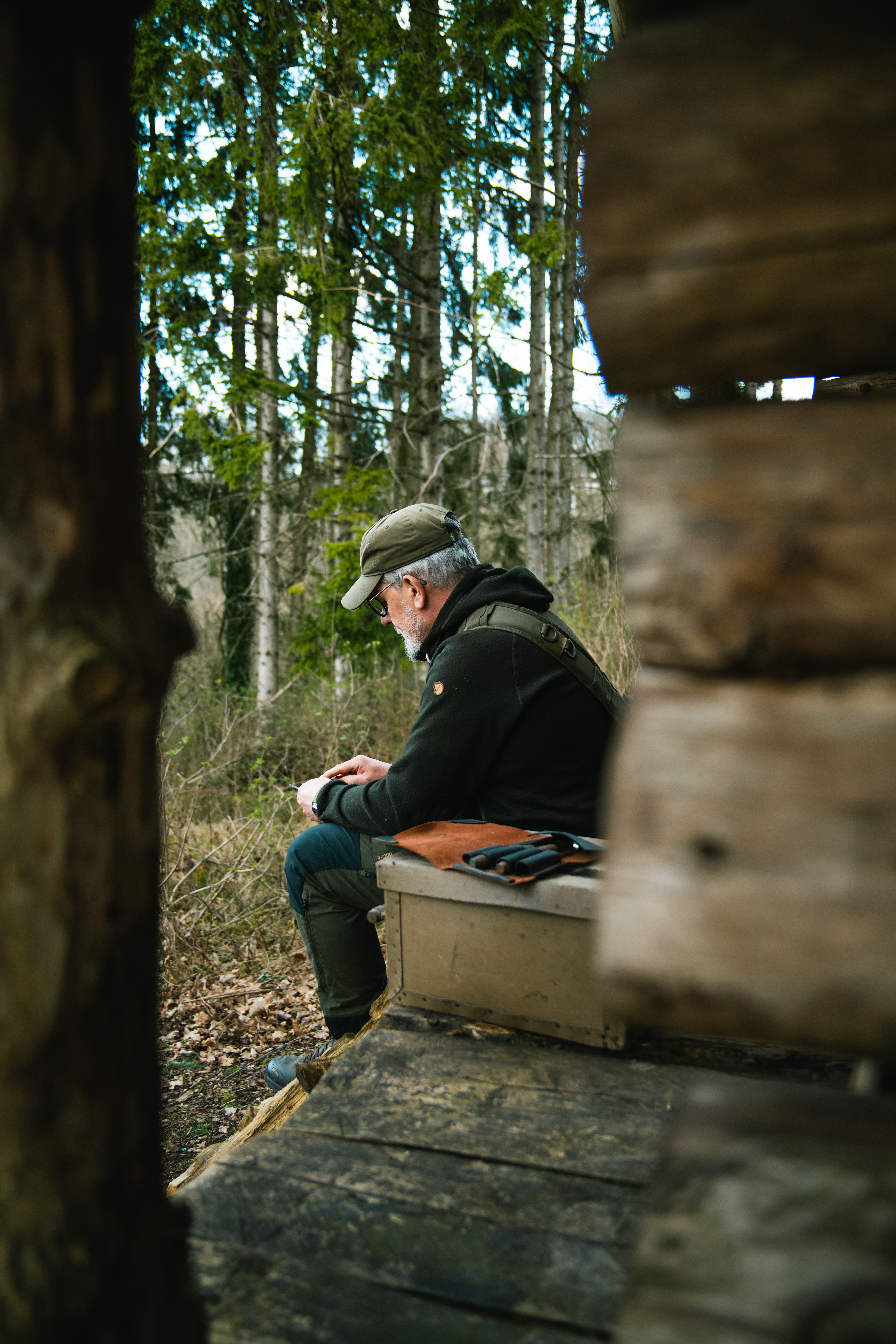Der Wildnispädagoge sitzt am Waldhäuschen und schnitzt.