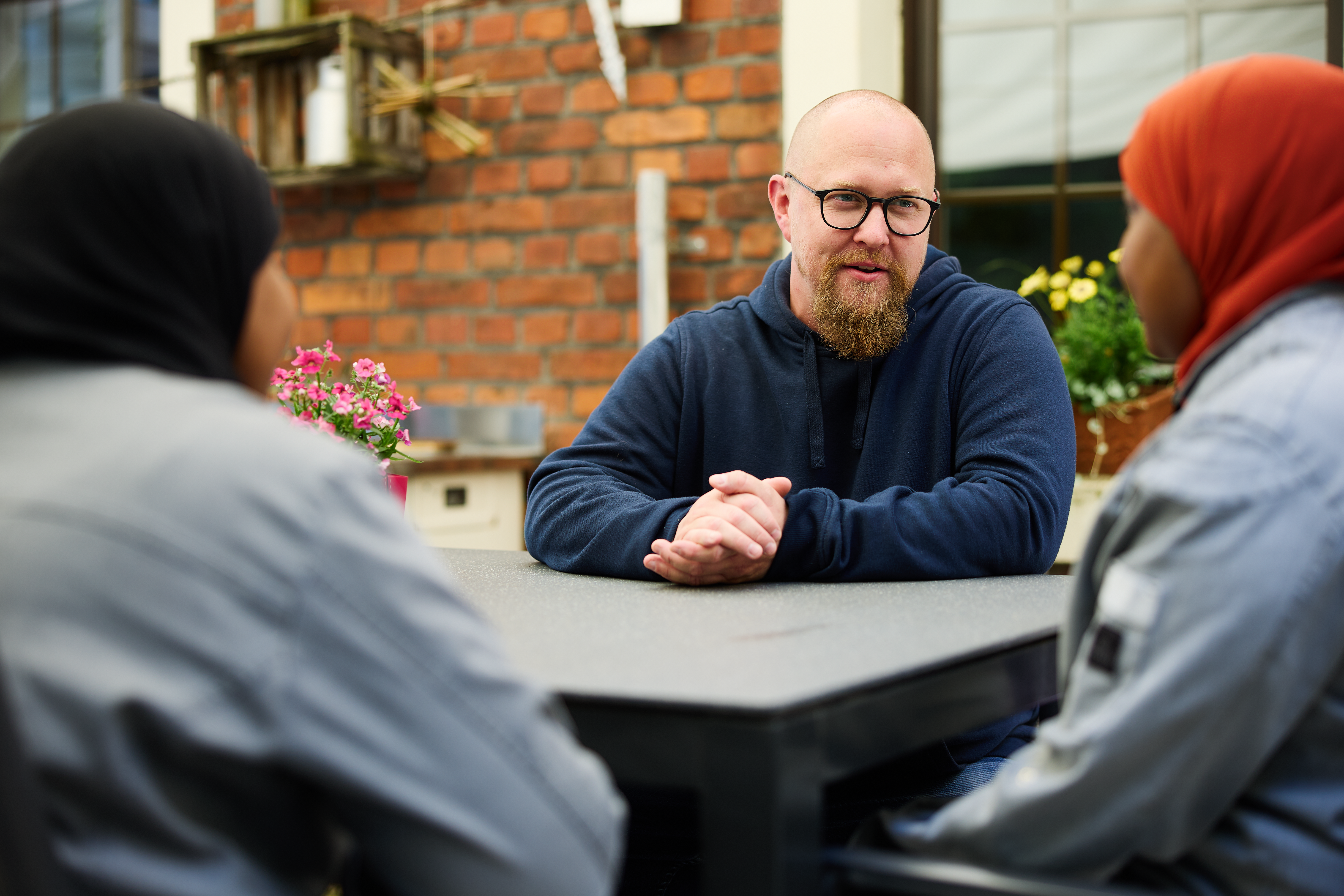 Zwei Frauen und ein Mann sitzen an einem Tisch, im Hintergrund das Haus Granat