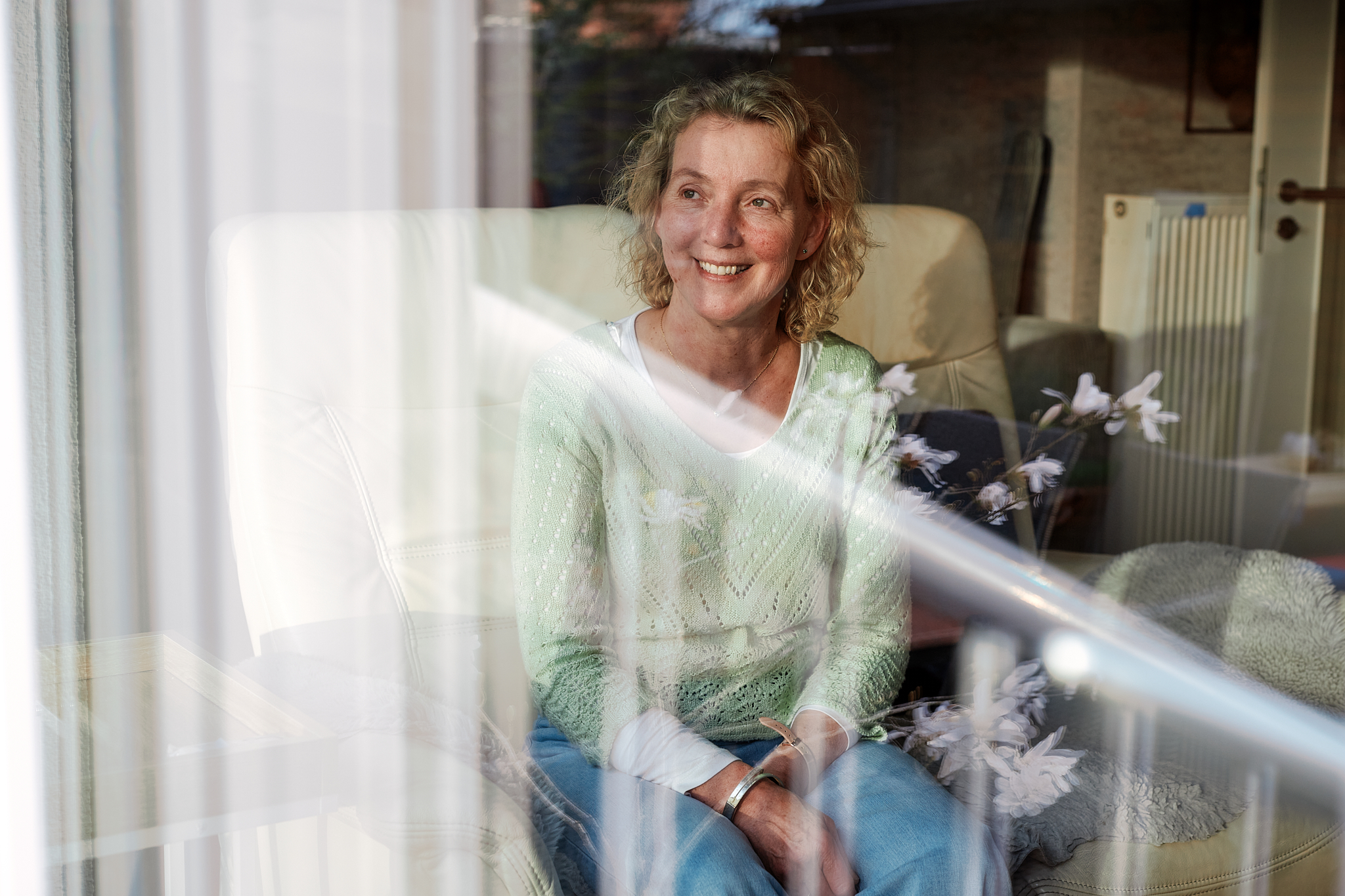 Eine Frau sitzt hinter einer Fensterscheibe und lächelt.