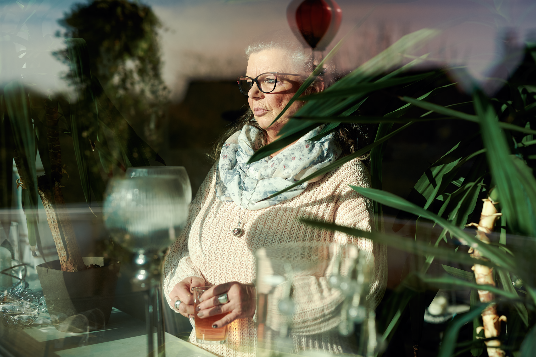 Ein Frau hält ein Glas Tee in den Händen und schaut aus dem Fenster.