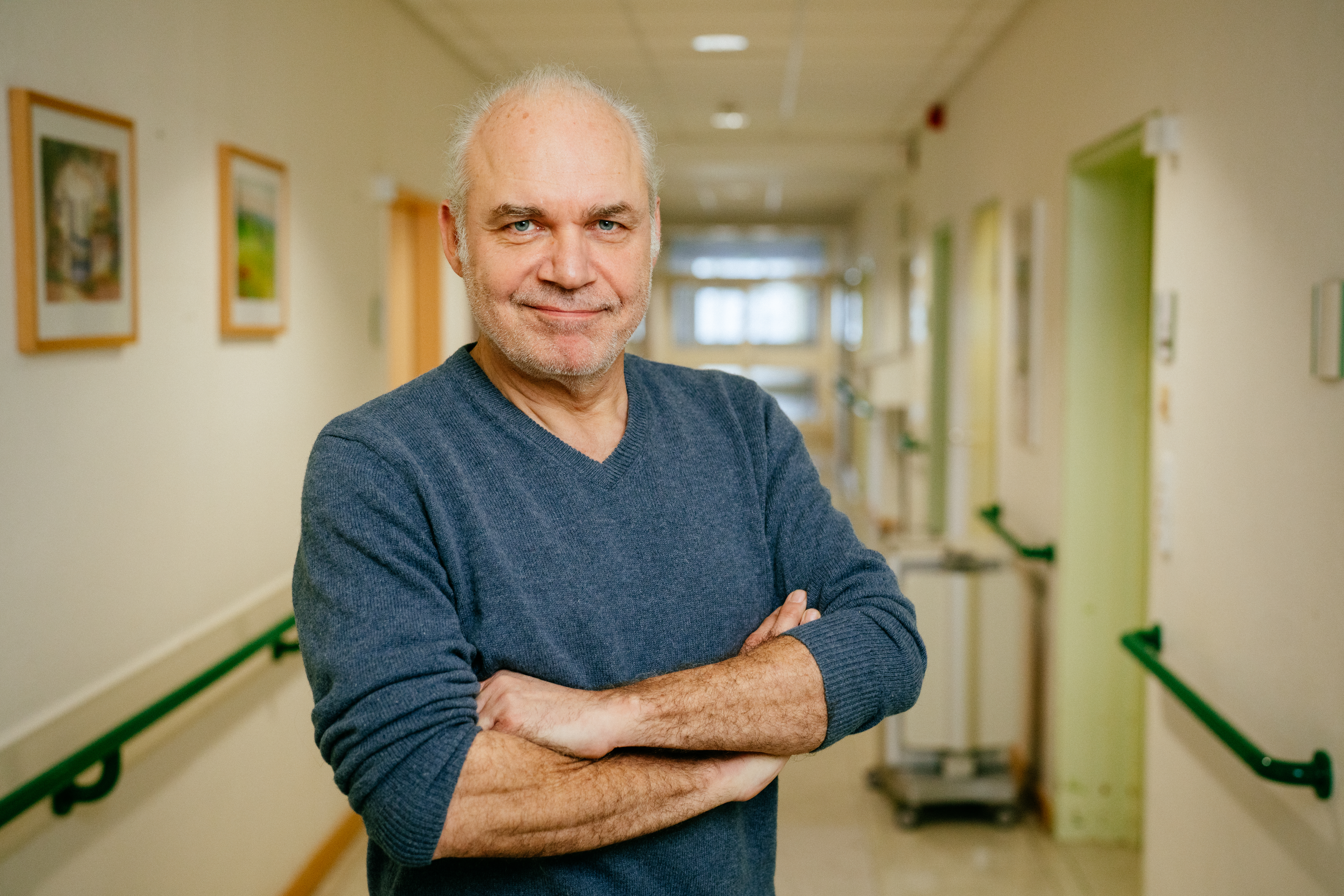 Porträt eines Mannes in grauem Pulli auf einem Krankenhausflur stehend.