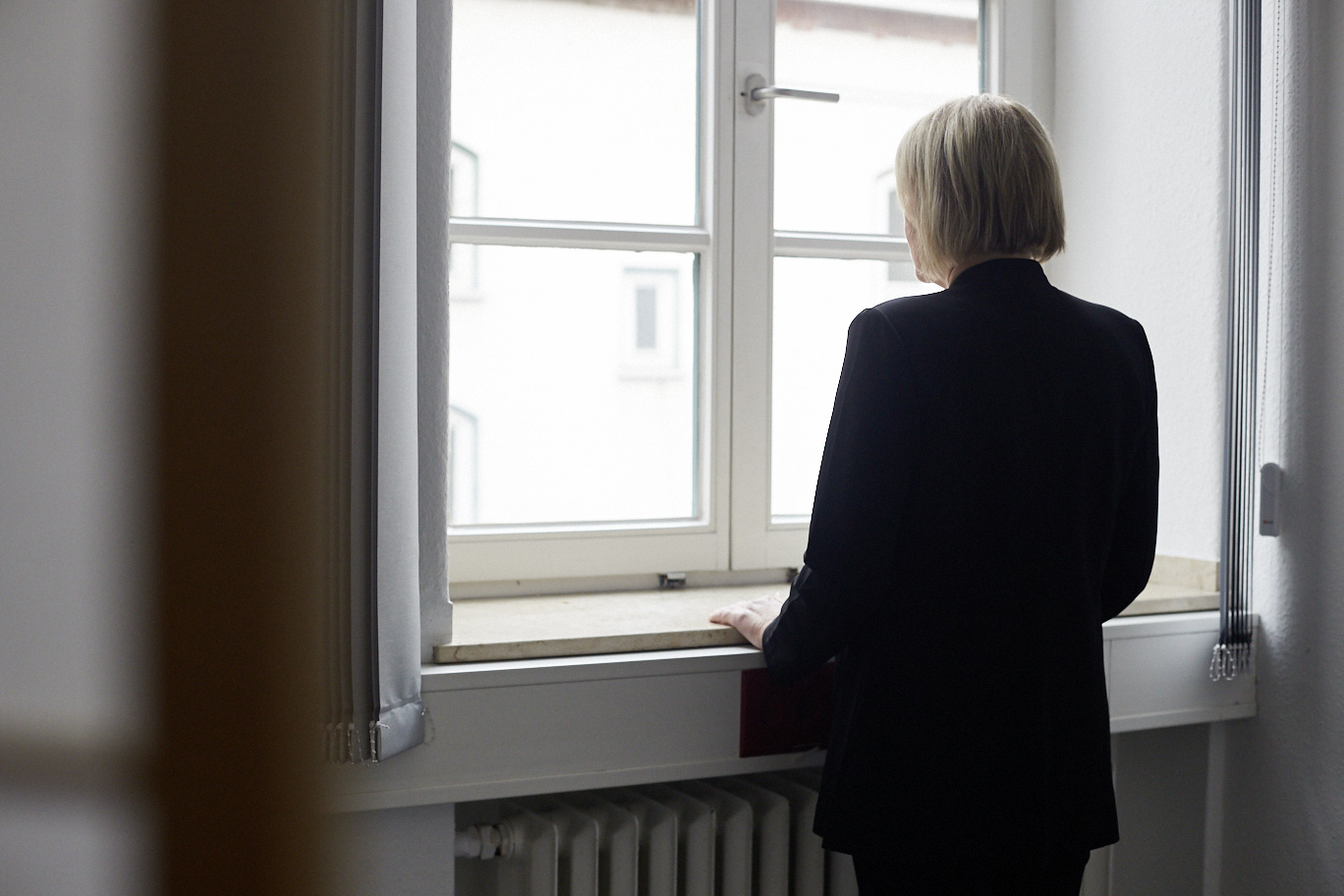 Eine Frau steht am Fenster und schaut nach draußen.