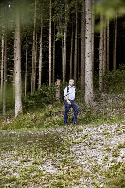Matthias Löb beim wandern vor einer Reihe von Baumstämmen.
