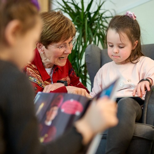 Frau mit rotem Blazer betrachtet mit einem Mädchen ein Kinderbuch