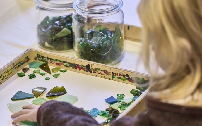 Kind ordnet grüne Glasscherben in einem Holzrahmen an.