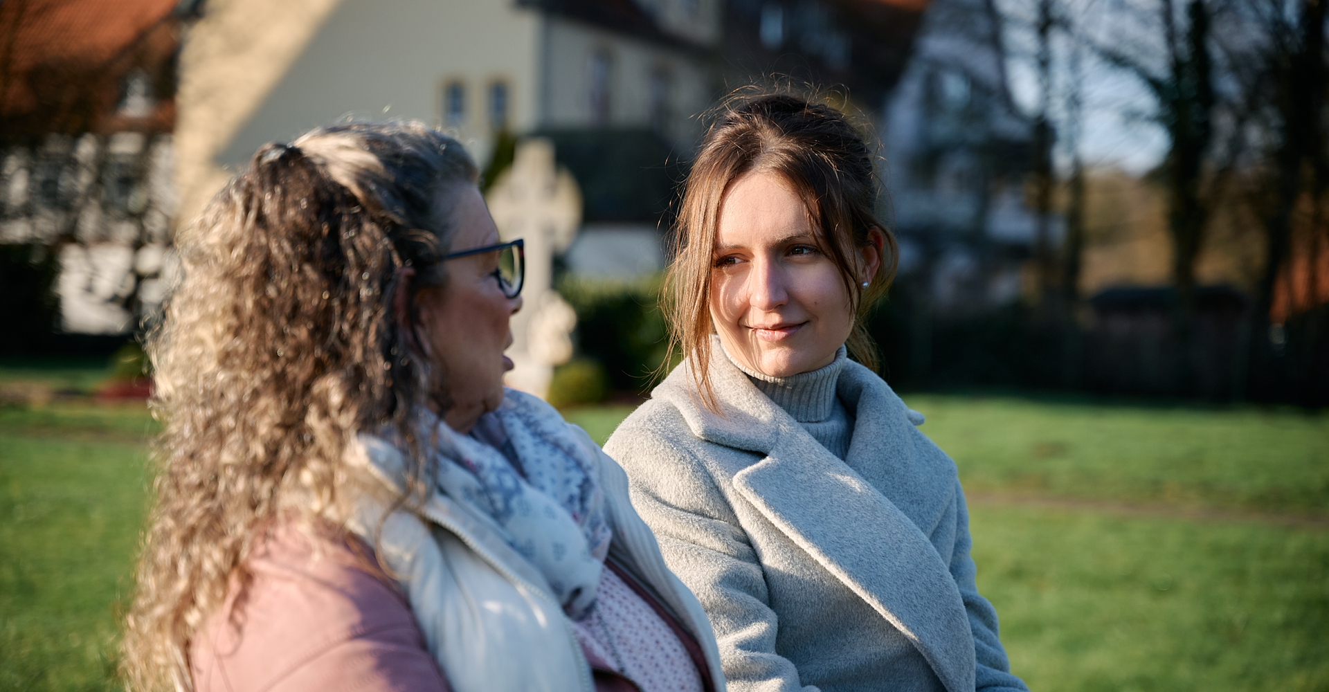 Zwei Frauen sitzen einander zugewandt auf einer Bank im Freien.