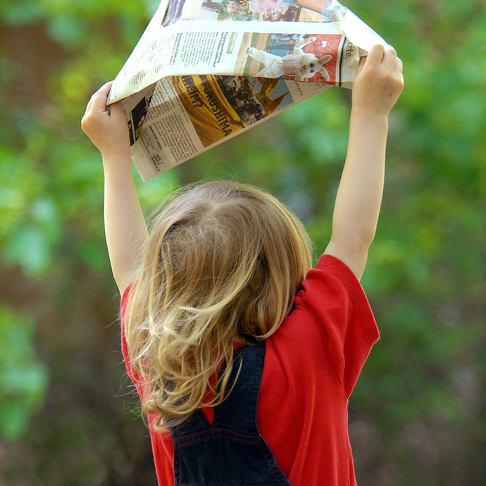 Ein Kind hält stolz seinen aus Zeitungspapier gebastelten Hut in die Höhe. (vergrößerte Bildansicht wird geöffnet)