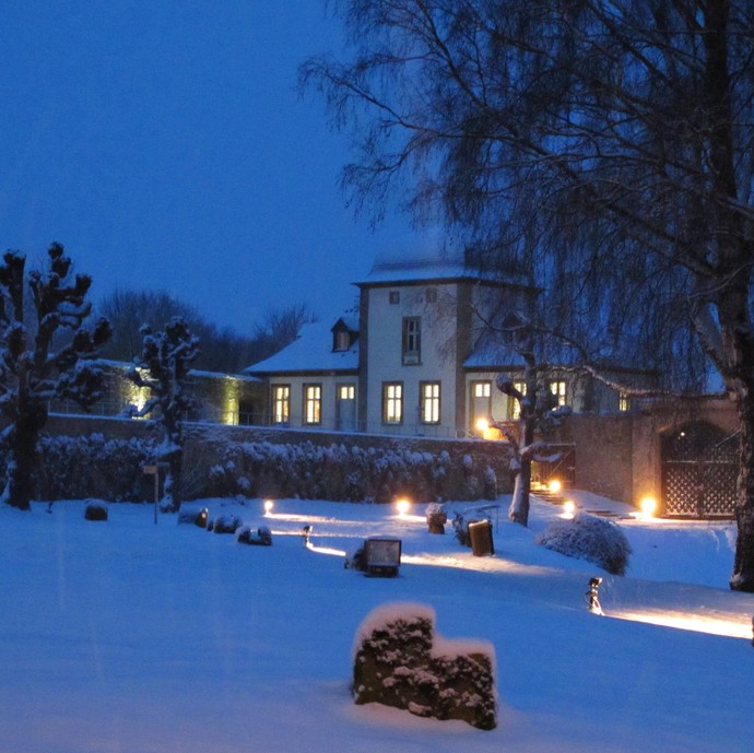 Das Kloster Dalheim von außen bei Nacht im Winter, umgeben von Bäumen. (vergrößerte Bildansicht wird geöffnet)
