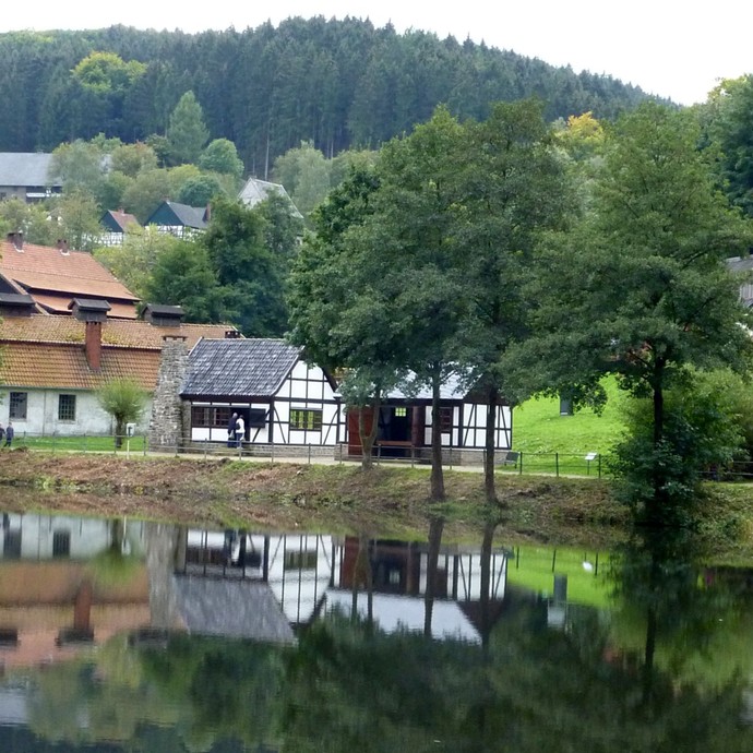 Blick über einen See auf alte Fachwerkhäuser, umgeben von vielen Bäumen (vergrößerte Bildansicht wird geöffnet)