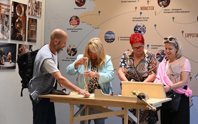 Vier Erwachsene stehen an einem Holztisch und probieren Angebote aus.