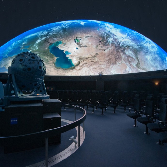Die Leinwand des Planetariums zeigt die Erde von oben. Im Vordergrund ist der Projektor zu sehen. (öffnet vergrößerte Bildansicht)