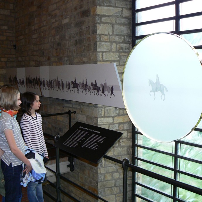 Zwei junge Mädchen stehen vor einer runden Glasscheibe, auf der eine Person auf einem Pferd aufgedruckt ist. (vergrößerte Bildansicht wird geöffnet)