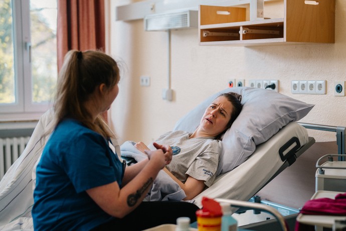 Eine junge Auszubildende sitzt am Bett einer Patientin.