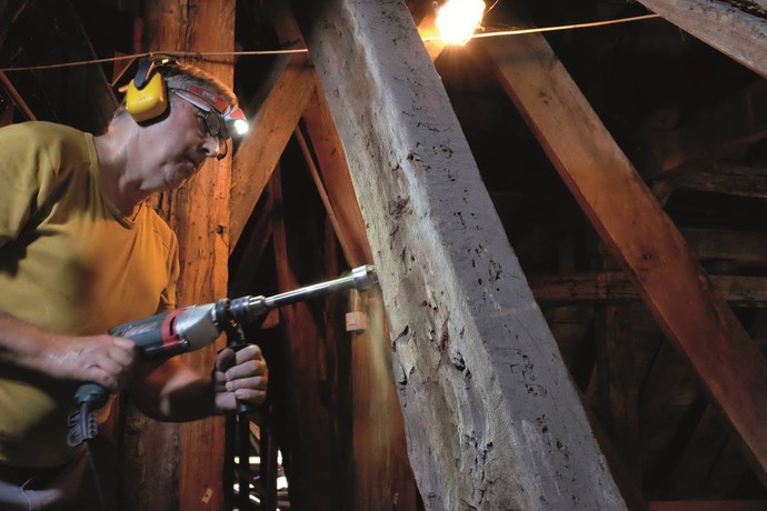 Ein Bauforscher entnimmt an einem mittelalterlichen Dachstuhl eine Probe für eine dendochronologische Untersuchung.