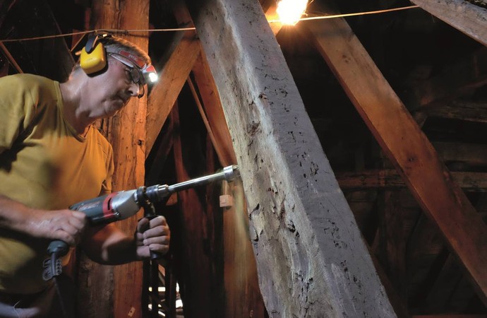 Ein LWL-Bauforscher entnimmt an einem mittelalterlichen Dachstuhl eine Probe für eine dendochronologische Untersuchung.