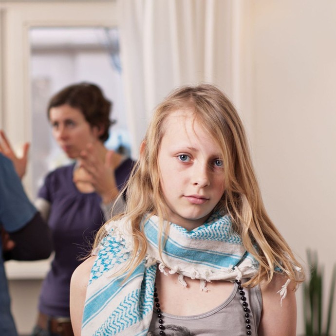 Während sih ihre Eltern im Hintergrund streiten schaut die Tochter traurig und hält ein Schild hoch, das eine glückliche Familie zeigt. (vergrößerte Bildansicht wird geöffnet)