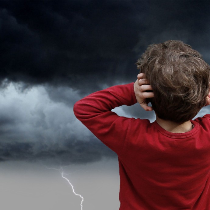 Ein kleiner Junge hält sich die Ohren zu, während in der Ferne ein dunkles Gewitter aufzieht. (vergrößerte Bildansicht wird geöffnet)