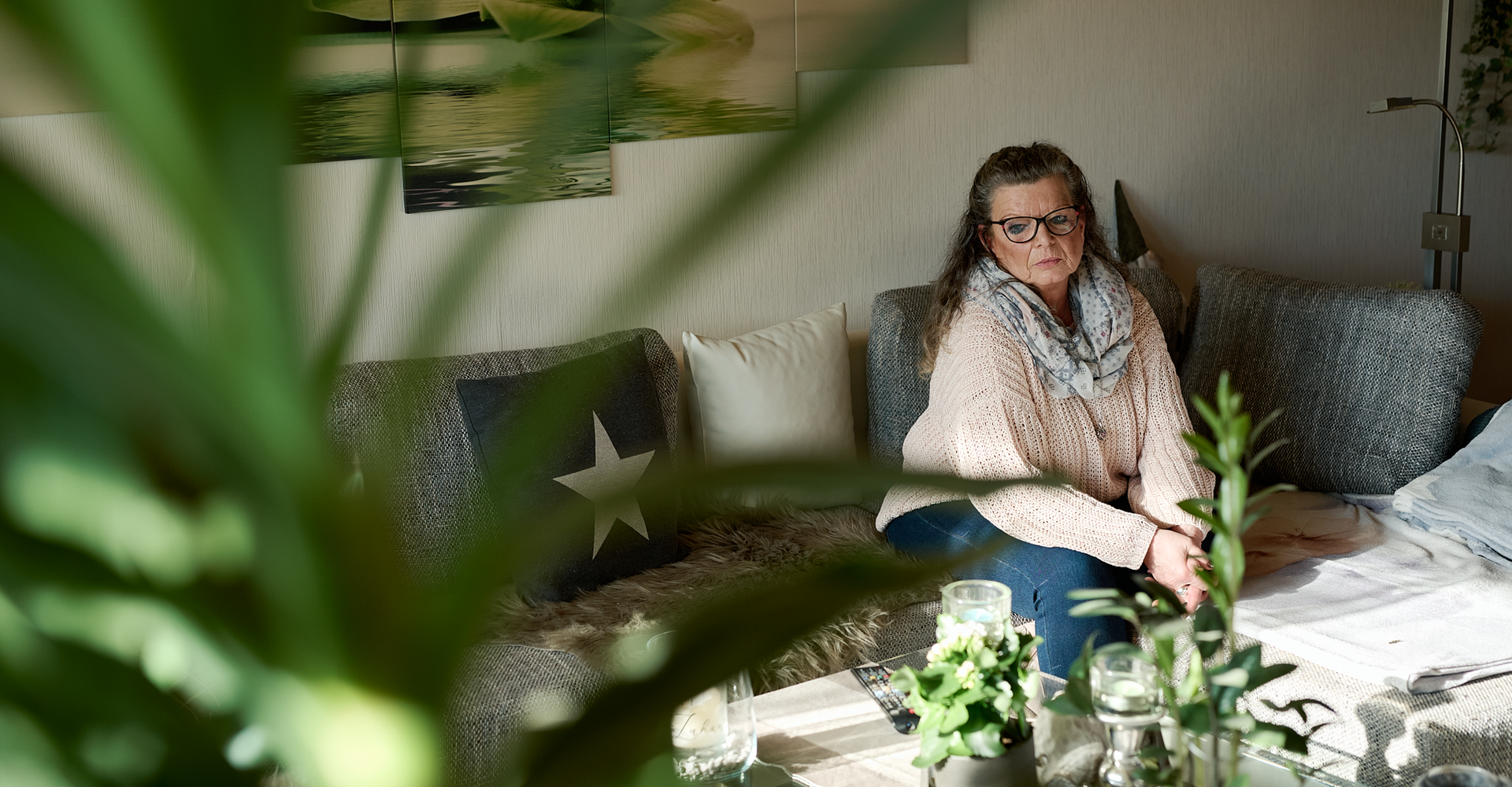Eine Frau sitzt nachdenklich im Wohnzimmer.