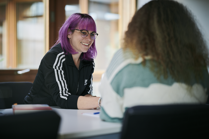 Zwei Frauen sitzen sich am Tisch gegenüber. Es sind Ilka Scholl und Büsra Cerny.