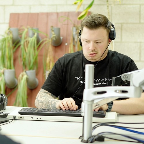 Ein junger Mann mit Kopfhörern verwendet eine Braillezeile.