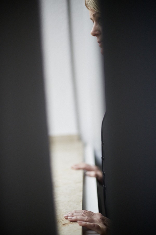 Das Foto zeigt eine Frau die am Fenster steht und nach draussen schaut.