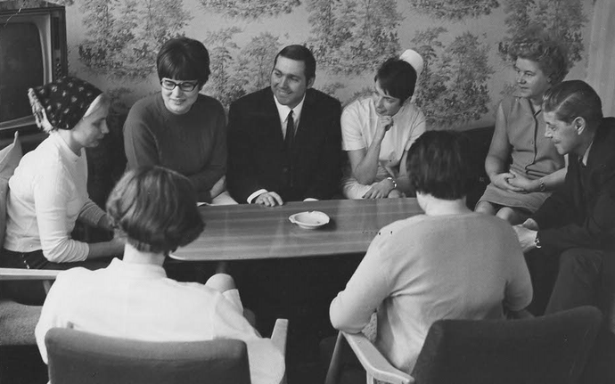 Eine Gruppe von Männern und Frauen, die im Gespräch mit einander um einen Tisch sitzen.