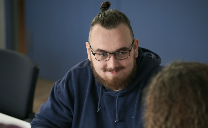 Ein Mann sitzt am Tisch und schaut eine Frau an, die ihm gegenüber sitzt. Die Frau sieht man nur von hinten.