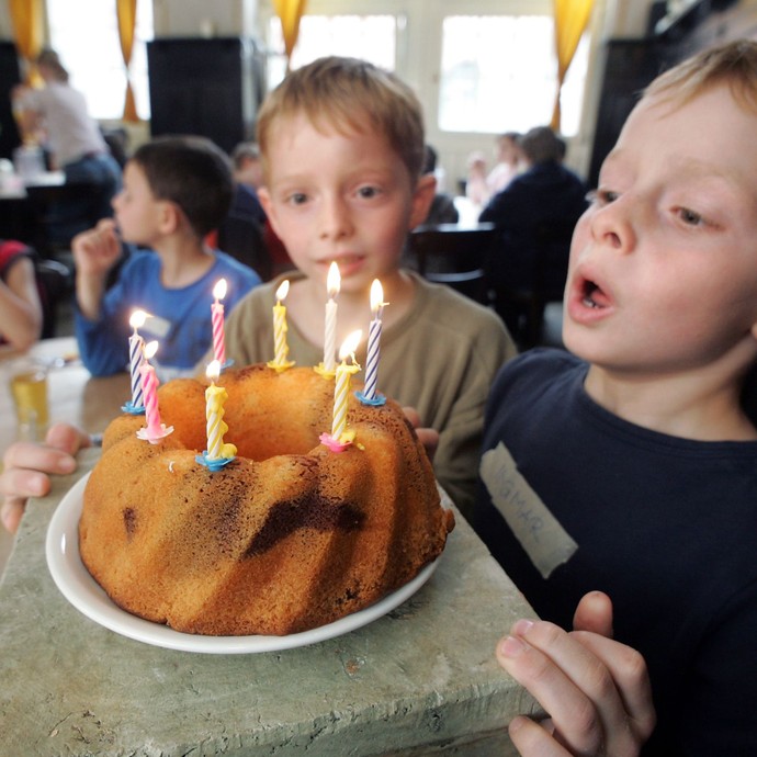 Ein Junge bläst Kerzen auf einem Kuchen aus. Im Hintergrund sind viele weitere Kinder (öffnet vergrößerte Bildansicht)