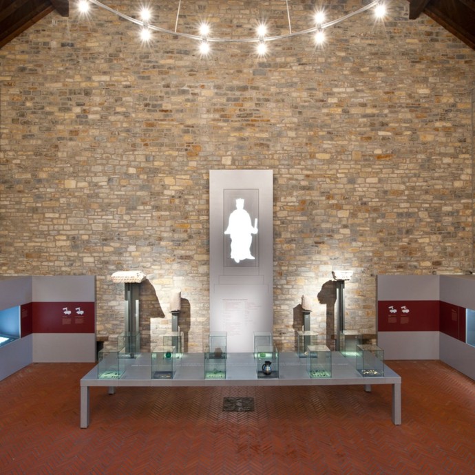 Ein großer Raum mit Steinmauern und rotem Tepich. Es sind viele Vitrinen zu sehen. (vergrößerte Bildansicht wird geöffnet)