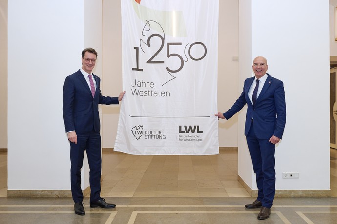 Dr. Georg Lunemann, der Direktor des LWL mit NRW-Ministerpräsident Hendrik Wüst neben der Flagge zum Jubiläum 1250 Jahre Westfalen.