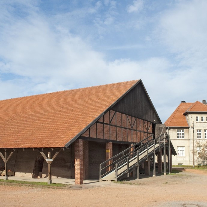 Blick auf ein altes Fachwerkhaus mit Schornstein mit einer Rampe in den ersten Stock. (vergrößerte Bildansicht wird geöffnet)