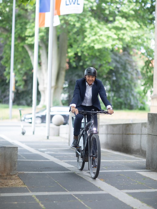 Dr. Georg Lunemann auf einem Fahrrad fahrend vor dem Eingang des Landeshauses. (vergrößerte Bildansicht wird geöffnet)