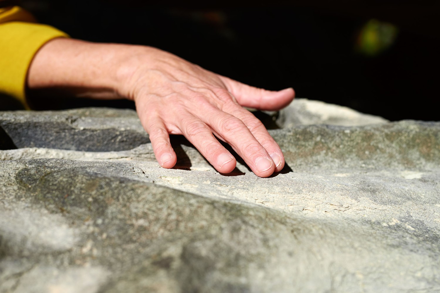 Eine Hand streicht über die verwitterte Kalksandsteinoberfläche