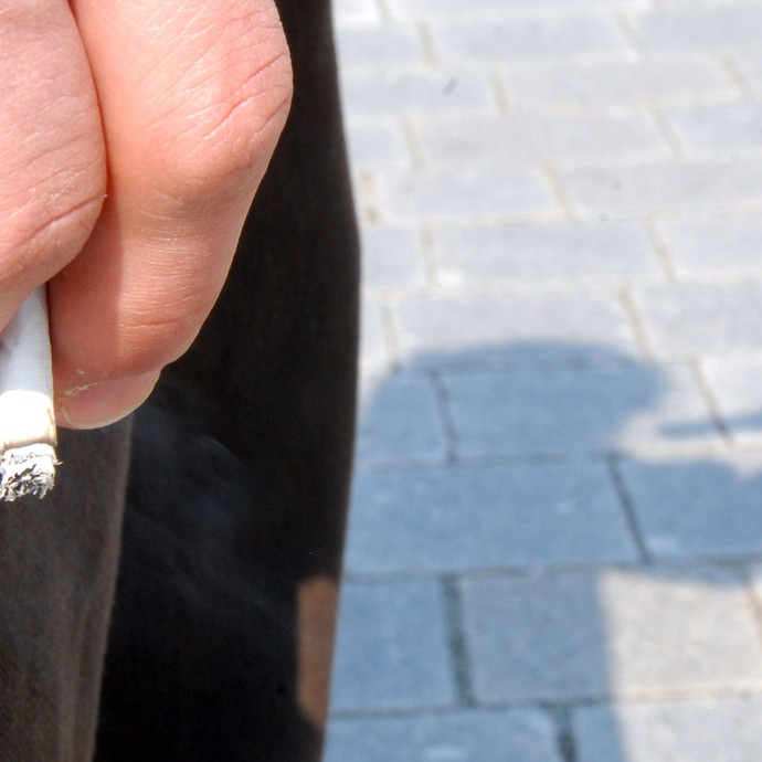 Eine Zigarette wird in einer Hand gehalten und im Hintergrund deutet eine Schatten auf Alkoholmissbrauch hin. (vergrößerte Bildansicht wird geöffnet)