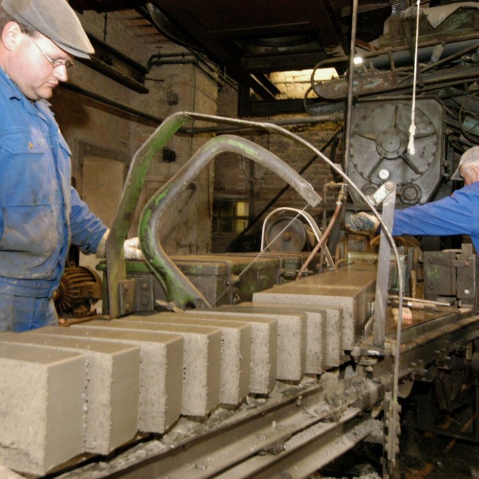Zwei Männern arbeiten an einer Stangpresse, an der Steinziegel hergestellt werden. (öffnet vergrößerte Bildansicht)