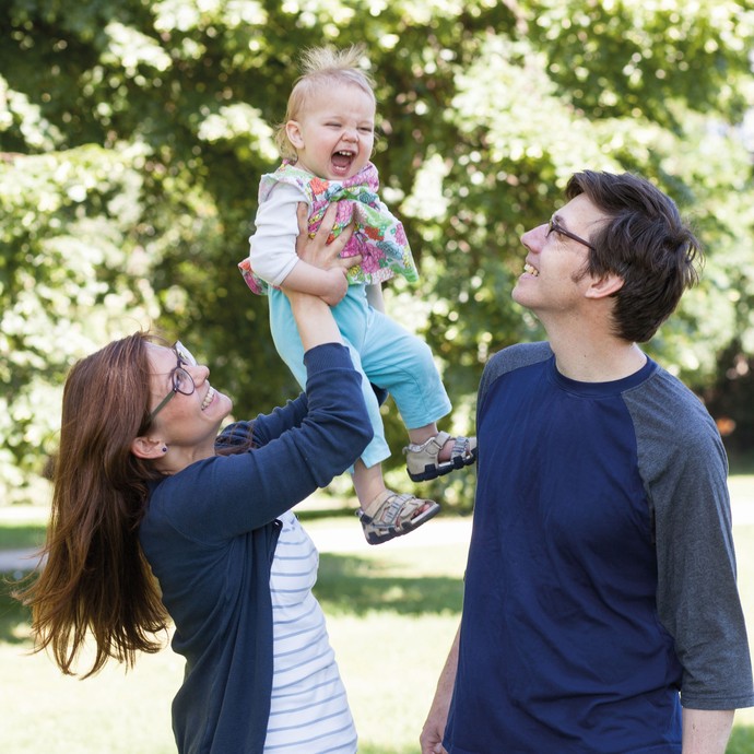 Eine Familie spielt mit ihrem Kind im Park. Die Mutter hält das lachende Mädchen in die Höhe. (vergrößerte Bildansicht wird geöffnet)