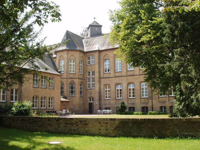 altes Gebäude des LWL-Pflegezentrums Lippstadt mit Turmuhr, davor ein Mauer und Bäume